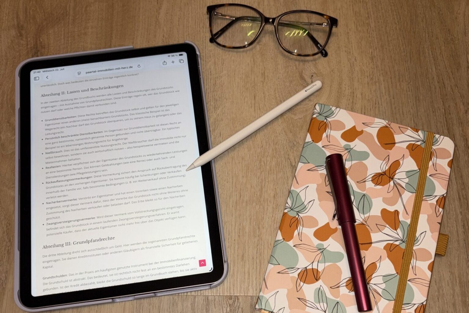 Das Grundbuch entschlüsselt: Was Eigentümer im Paartal über Abteilung II und III wissen müssen Ein iPad auf einem Holztisch zeigt den geöffneten Paartal-Blogeintrag über das Grundbuch, daneben liegt eine Brille und ein Notizbuch.